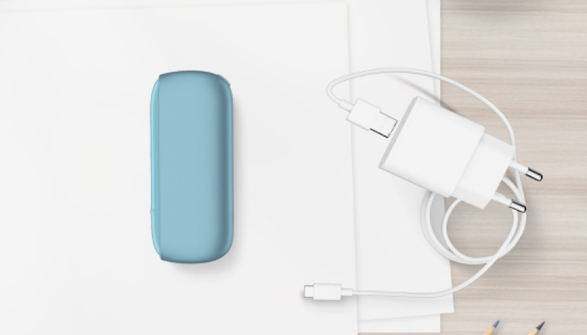 شاحن جيب جهاز IQOS ORIGINALS DUO بلون التركواز بجانب كابل الشحن.